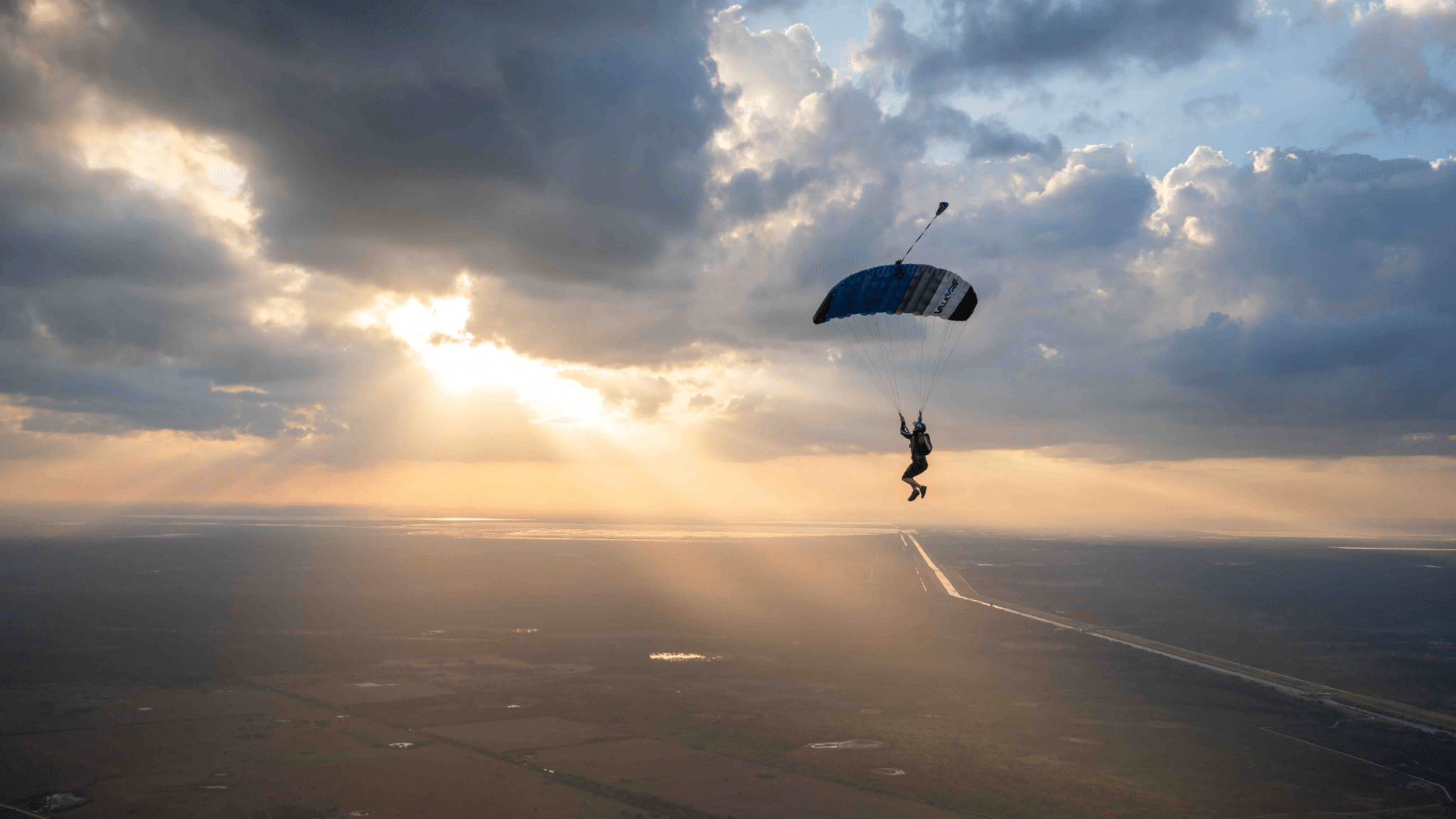 Skydiver under canopy with puffy clouds and the sun shining through